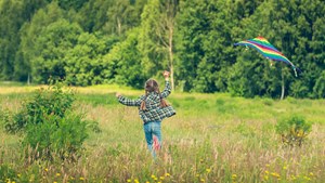 En pige løber med en drage i en mark